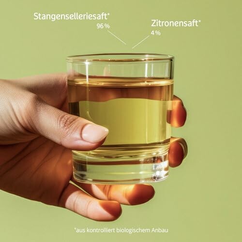 Hand hält ein Glas mit Stangenselleriesaft und Zitronensaft.