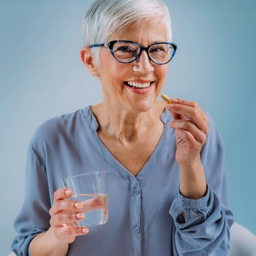Ältere Frau mit Brille hält eine Pille und ein Glas Wasser.